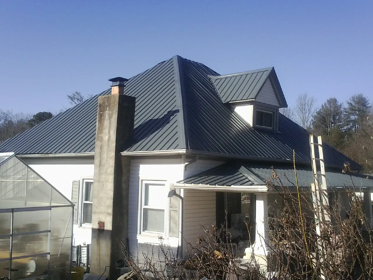 Dark blue standing seam metal roof on a white farmhouse with dormer — Slate & Tile Roof Repair by Roofing Brothers in Tomah