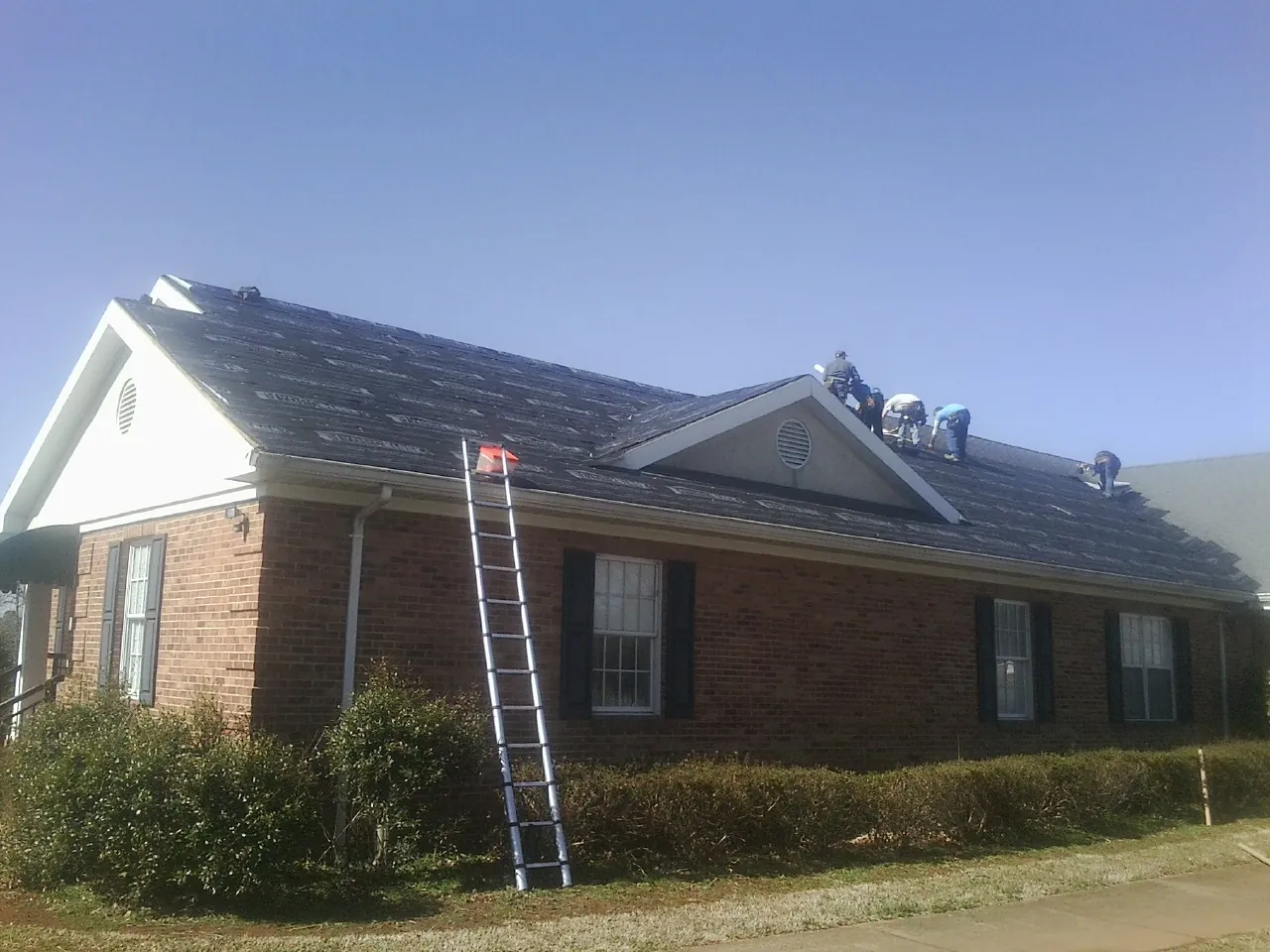 Crew tearing shingles off a brick ranch roof with a ladder set — Emergency Roof Repair work by our crew in Tomah