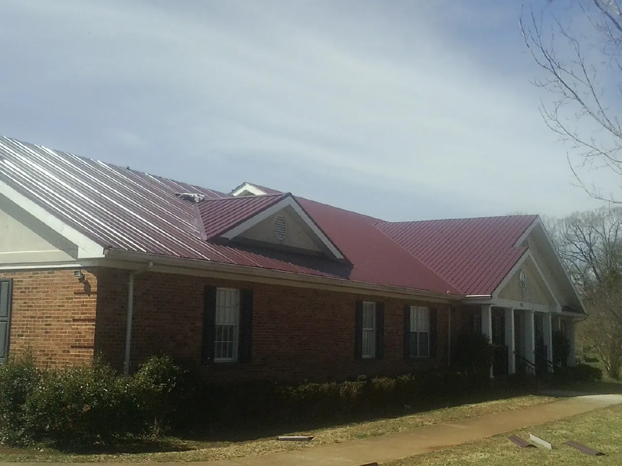 Red metal roof with gabled entries on a long brick building, from a Hail Damage Roof Repair job in Tomah