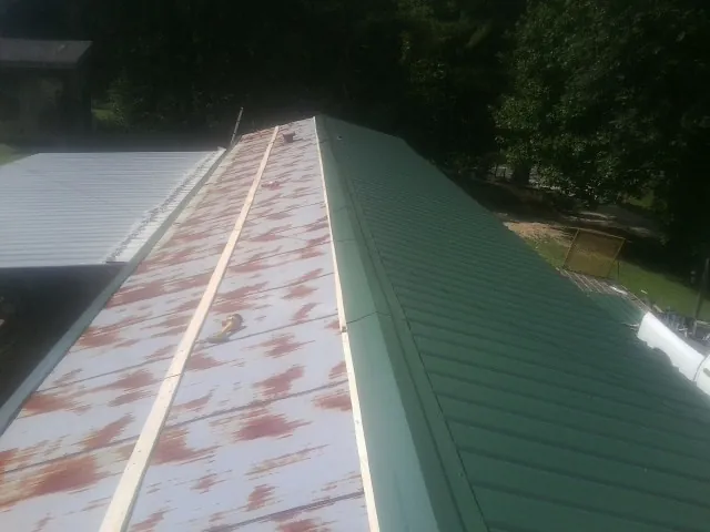 Old rusted panels beside newly installed green metal roofing — Wind Damage Roof Repair by Roofing Brothers in Tomah