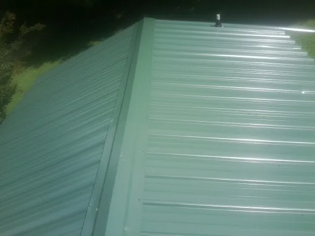 New green metal panels meeting at the ridge of a roof — Flat Roof Repair work by our crew in Tomah