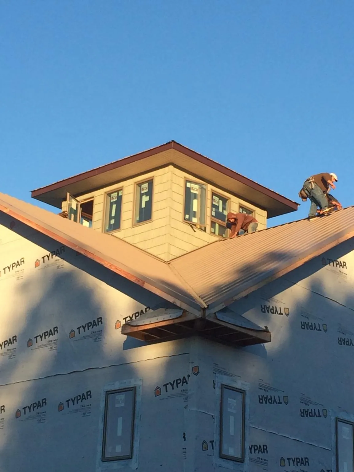 Roofers working around a rooftop cupola on a new metal roof at sunset — Roof Waterproofing in Tomah by Roofing Brothers